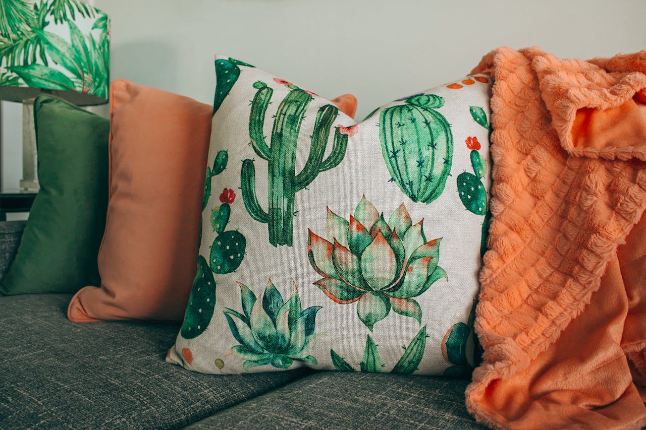 A stylish living room setup with cactus-themed pillow and soft orange blanket.