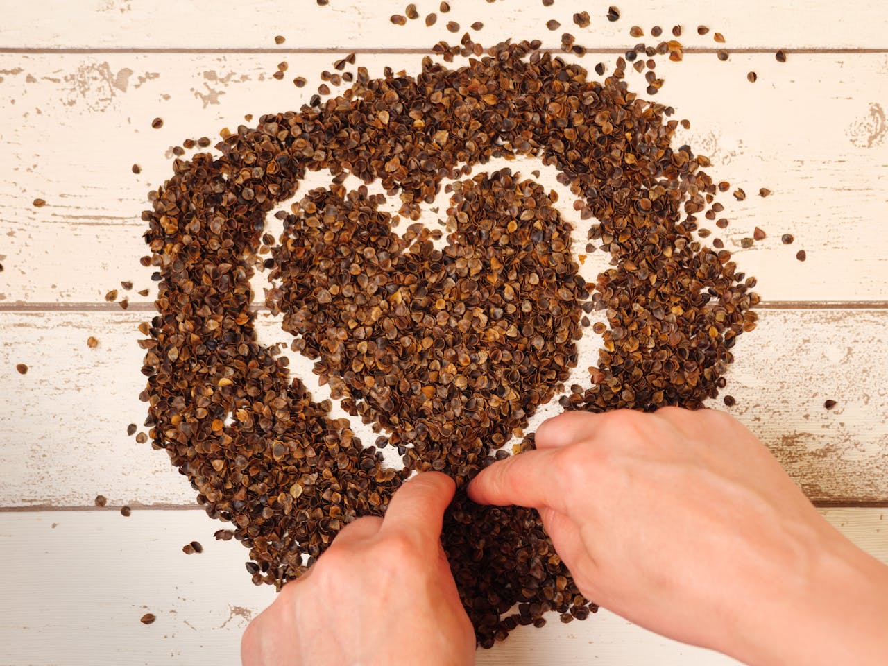 Hands form a heart shape with buckwheat husks on a rustic wooden background, symbolizing love for nature.