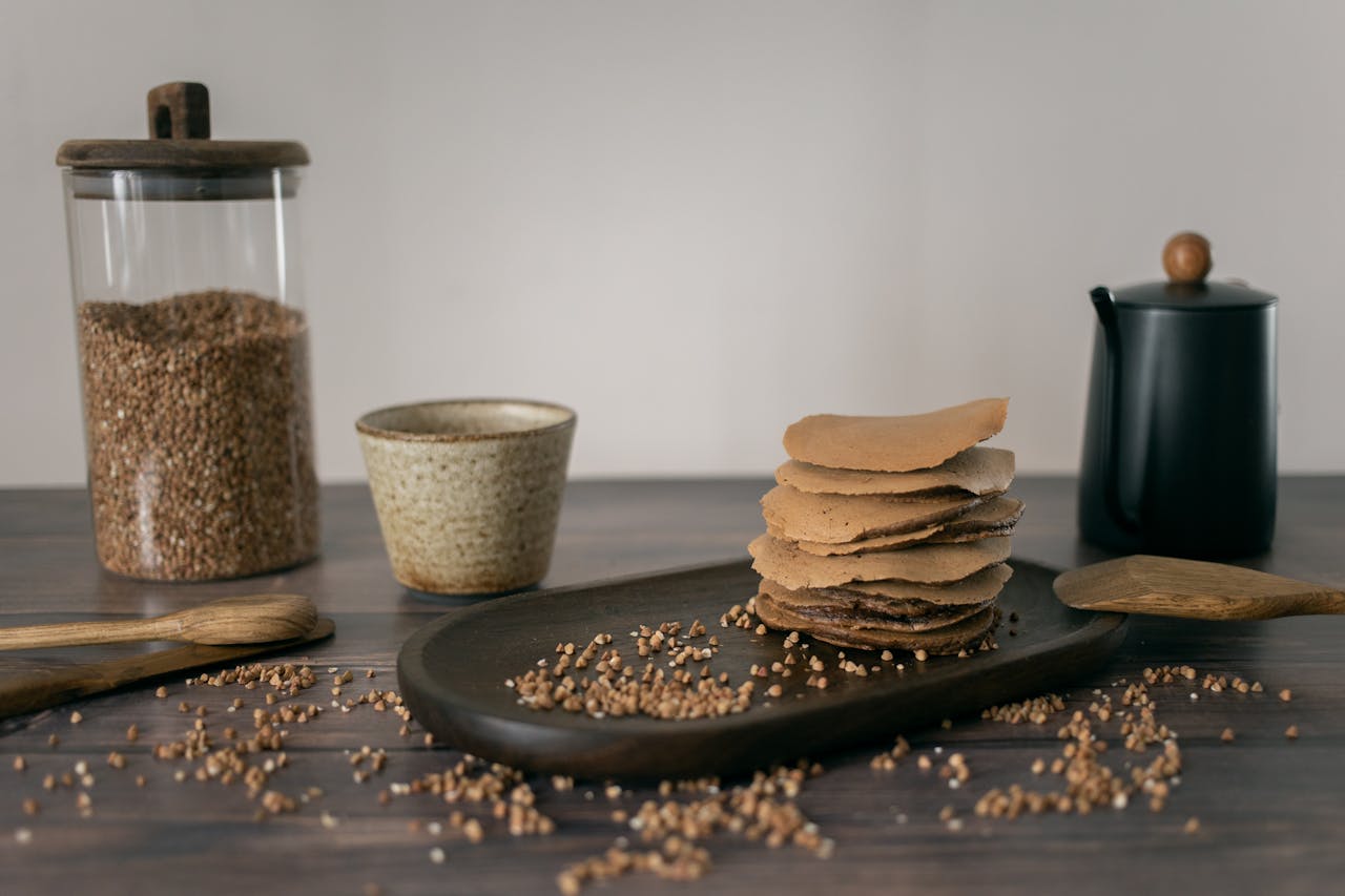 A rustic arrangement of buckwheat pancakes with kitchen tools and ingredients on a wooden table.