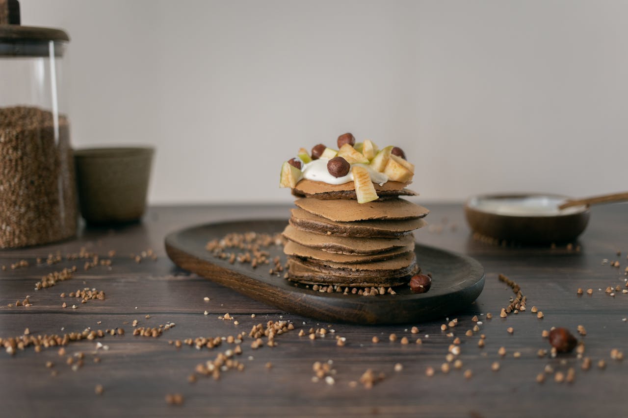 Delicious buckwheat pancakes topped with fruits and nuts on a rustic wooden table.